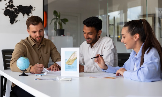 Three travel agents sitting at a desk in a modern office, smiling and discussing documents, with a globe and travel brochure visible on the table