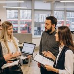 Office team discussing a project with a laptop and documents in a modern workplace setting with windows in the background